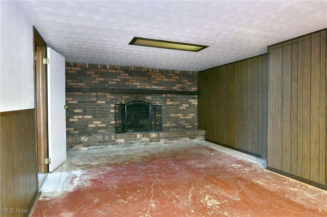Unfurnished living room featuring baseboards, a textured ceiling, wooden walls, and a fireplace | Image 38