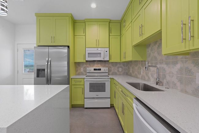 Kitchen with backsplash, a sink, green cabinets, light stone countertops, and white appliances | Image 16