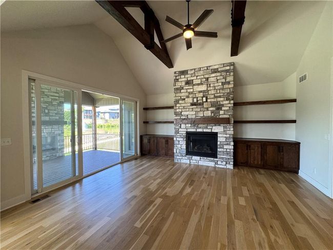 Unfurnished living room with wood finished floors, a ceiling fan, high vaulted ceiling, and a stone fireplace | Image 9