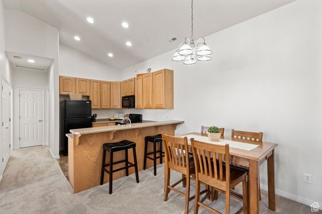 Kitchen with a kitchen breakfast bar, a peninsula, light countertops, light colored carpet, and black appliances | Image 7