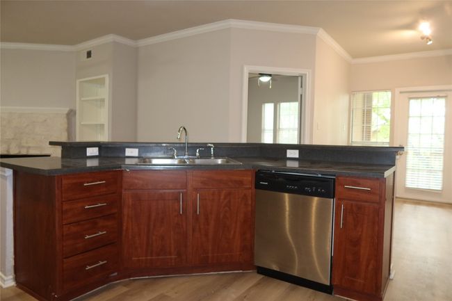 Kitchen with stainless steel dishwasher, a sink, light wood finished floors, dark countertops, and ornamental molding | Image 8