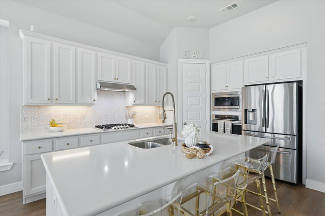 Kitchen featuring appliances with stainless steel finishes, under cabinet range hood, white cabinetry, backsplash, and dark wood-type flooring | Image 8