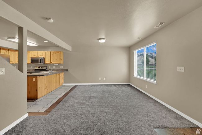 Kitchen with light brown cabinets, light carpet, appliances with stainless steel finishes, a peninsula, and light tile patterned floors | Image 7
