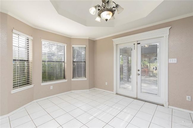 Dining room with French doors, a chandelier, a tray ceiling, and crown molding, exits to back patio. | Image 11
