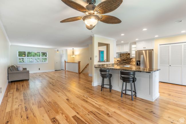 Kitchen featuring a kitchen breakfast bar, dark stone countertops, ornamental molding, stainless steel fridge, and white cabinetry | Image 4