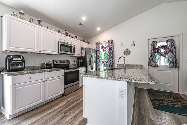 Kitchen featuring stainless steel appliances, vaulted ceiling, a sink, a peninsula, and wood finished floors | Image 7