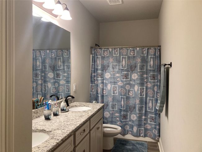 Bathroom featuring a shower with curtain, double vanity, toilet, a sink, and visible vents | Image 11
