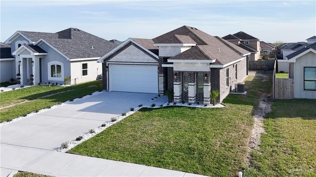 View of front of home with concrete driveway, stone siding, an attached garage, a front lawn, and central AC | Image 8