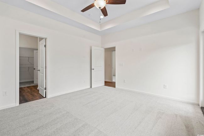 Unfurnished bedroom with carpet flooring, baseboards, a tray ceiling, a walk in closet, and ceiling fan | Image 18