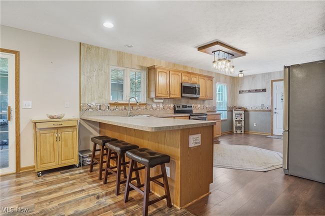 Kitchen with a sink, stainless steel appliances, a breakfast bar area, a peninsula, and wood finished floors | Image 14