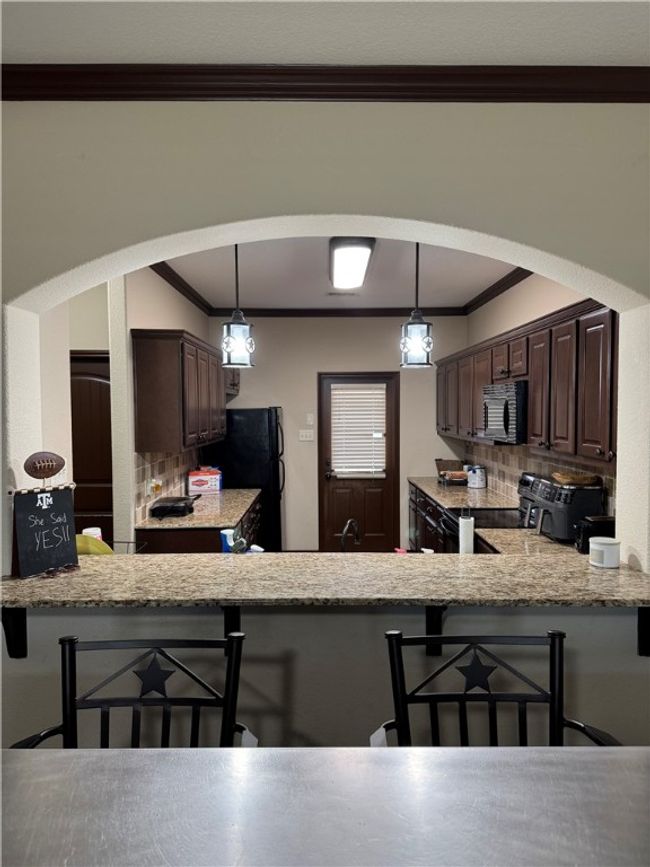 Kitchen featuring black appliances, dark brown cabinets, crown molding, a breakfast bar area, and backsplash | Image 15
