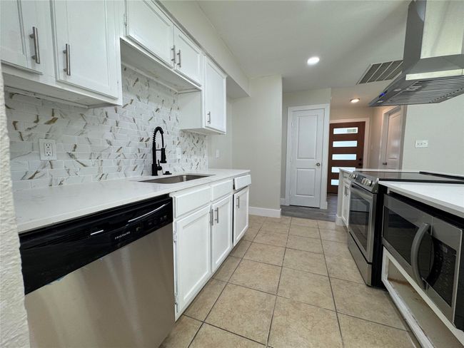 Kitchen featuring light tile patterned floors, backsplash, wall chimney exhaust hood, stainless steel appliances, and a sink | Image 8