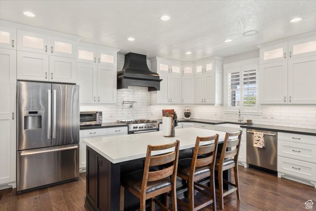 Kitchen with custom exhaust hood, dark wood finished floors, backsplash, and stainless steel appliances | Image 16