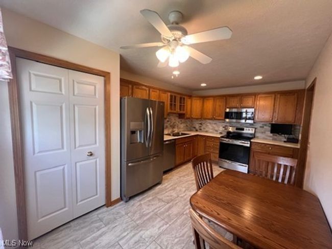 Kitchen with stainless steel appliances, brown cabinets, ceiling fan, tasteful backsplash, and light countertops | Image 4