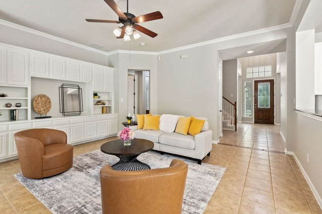 Living room with crown molding, light tile patterned floors, a ceiling fan, stairs, and built in features | Image 17