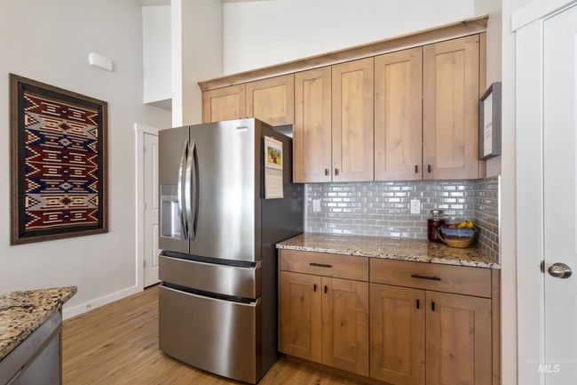 Kitchen with stainless steel refrigerator with ice dispenser, backsplash, light wood-type flooring, and light stone counters | Image 6