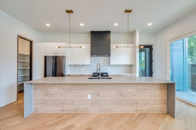 Kitchen featuring freestanding refrigerator, wall chimney exhaust hood, modern cabinets, a large island, and white cabinets | Image 8