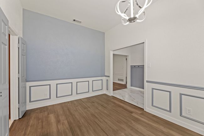 Unfurnished dining area with a wainscoted wall, a decorative wall, visible vents, a chandelier, and wood finished floors | Image 6
