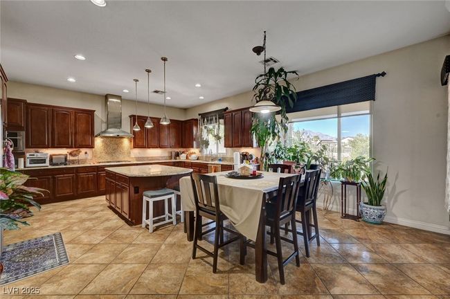Kitchen featuring wall chimney exhaust hood, a center island, stainless steel gas stovetop, a breakfast bar area, and recessed lighting | Image 21