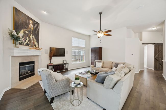 Vaulted ceilings and wide-plank wood floors enhance the sense of space in this central living room, anchored by a gas fireplace and framed by light from dual windows. | Image 11