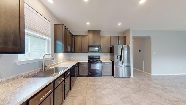 Kitchen featuring dark brown cabinets, a sink, light countertops, arched walkways, and black appliances | Image 18