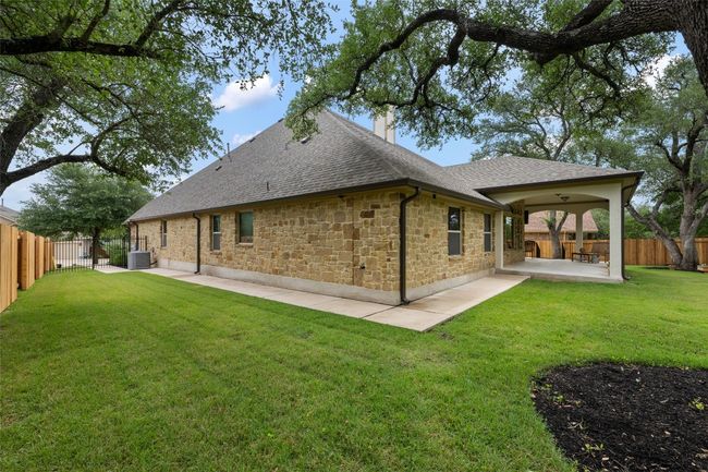 Rear view of property with a shingled roof, a patio, a chimney, a fenced backyard, and stone siding | Image 35