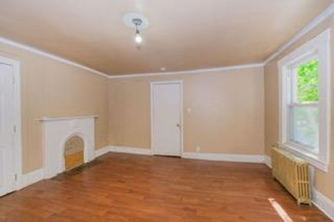Unfurnished living room with radiator, crown molding, wood finished floors, and a fireplace | Image 26
