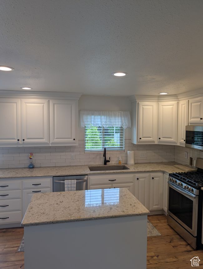 Kitchen featuring appliances with stainless steel finishes, a sink, backsplash, white cabinets, and a textured ceiling | Image 12