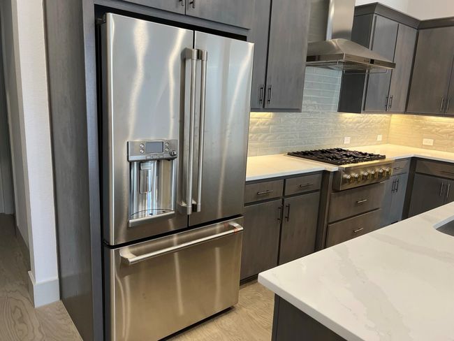 Kitchen featuring appliances with stainless steel finishes, wall chimney exhaust hood, decorative backsplash, and light stone countertops | Image 7