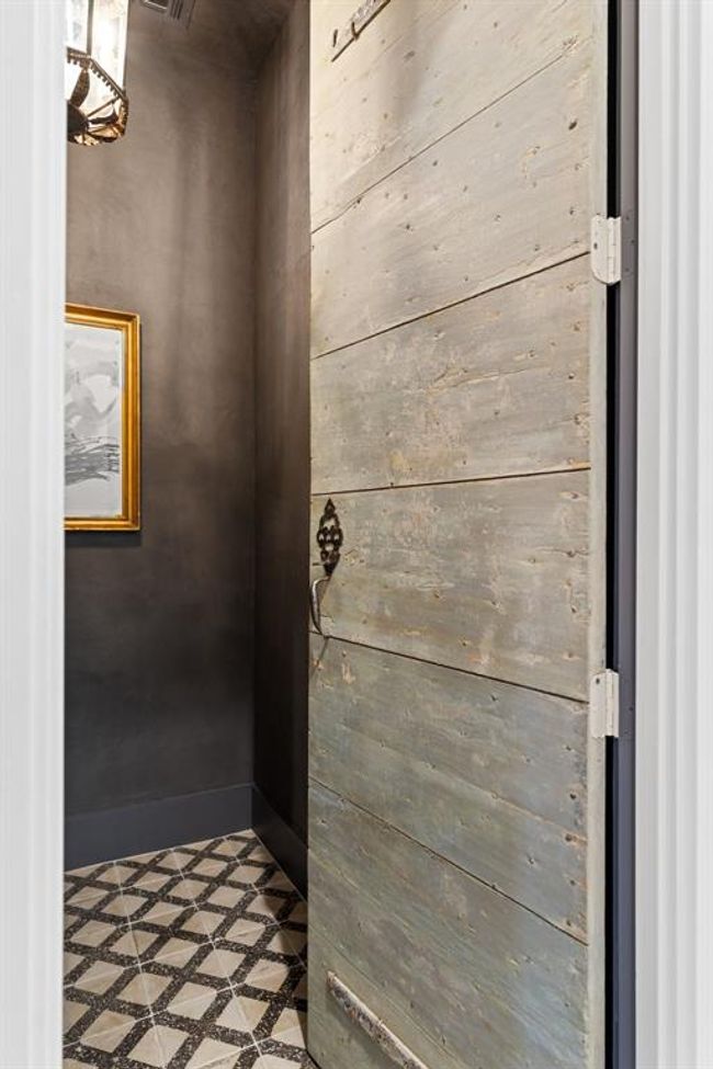 This antique wood door features original rustic hardware and a finish that complements the home. Reclaimed terrazzo tile adds a boldness and crisp component to the powder room. | Image 16