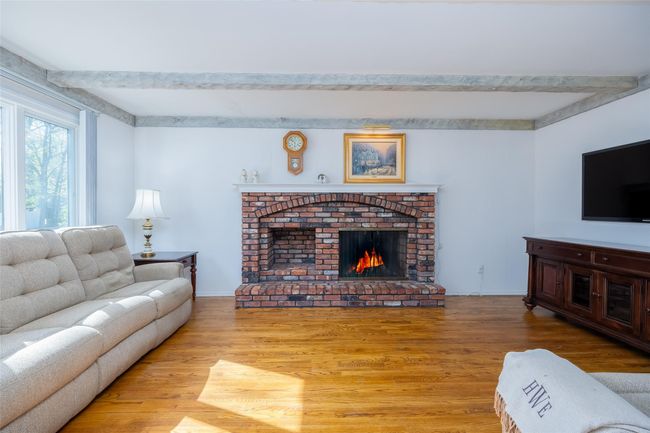 Living area with baseboards, beamed ceiling, wood finished floors, and a fireplace | Image 6