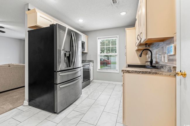 Kitchen featuring stainless steel appliances, light marble finish flooring, a textured ceiling, cream cabinetry, and tasteful backsplash | Image 7