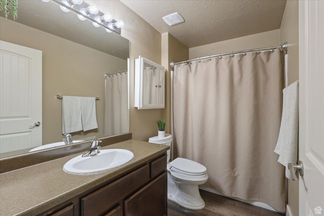 Bathroom featuring wood finished floors, a shower with shower curtain, toilet, vanity, and a textured ceiling | Image 11