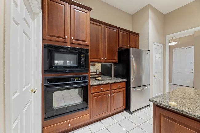 Kitchen with black appliances, light tile patterned floors, light stone counters, and decorative backsplash | Image 16