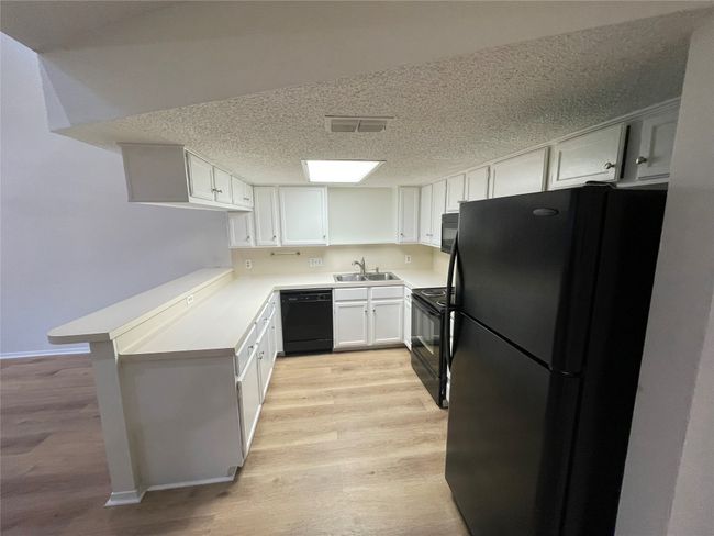 Kitchen with light hardwood / wood-style floors, kitchen peninsula, black appliances, white cabinets, and sink | Image 6