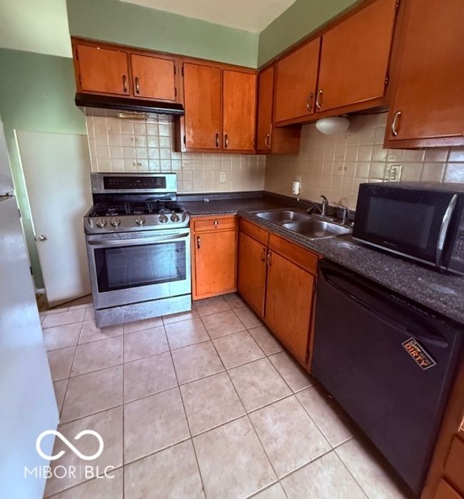 Efficient kitchen with stainless steel gas range, tile flooring, and ample cabinet storage-ready for everyday cooking or your next design update. | Image 6