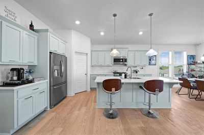 Kitchen with light wood-type flooring, stainless steel appliances, hanging light fixtures, and backsplash | Image 3