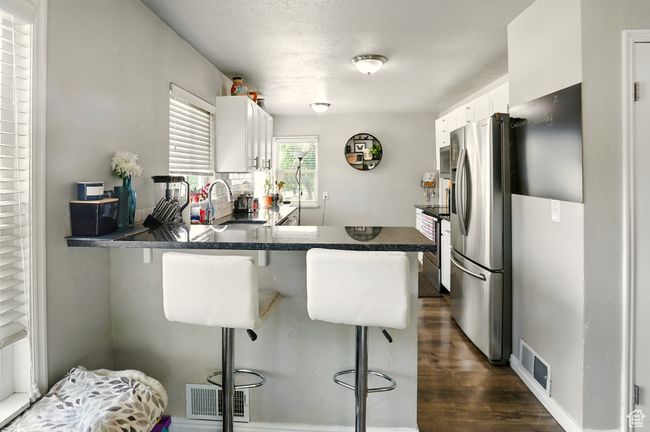 Kitchen featuring stainless steel appliances, white cabinets, dark wood-style floors, a peninsula, and a kitchen breakfast bar | Image 6