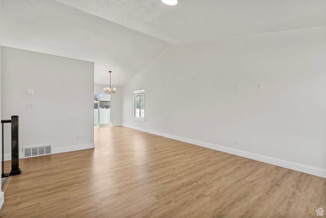 Unfurnished living room with a chandelier, light wood-type flooring, and lofted ceiling | Image 9