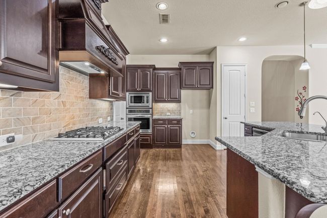Kitchen with appliances with stainless steel finishes, a sink, custom range hood, light stone counters, and recessed lighting | Image 12