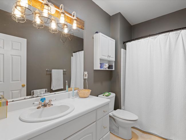 Full bath featuring a shower with shower curtain, a notable chandelier, toilet, and vanity | Image 30