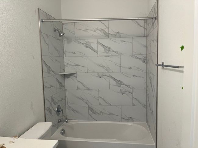 Bathroom with toilet, vanity, a textured wall, and bathtub / shower combination | Image 6
