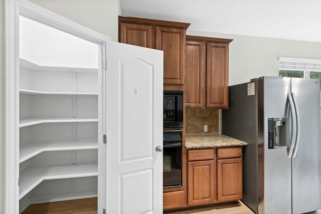 Kitchen featuring black appliances, backsplash, brown cabinetry, and light stone counters | Image 14