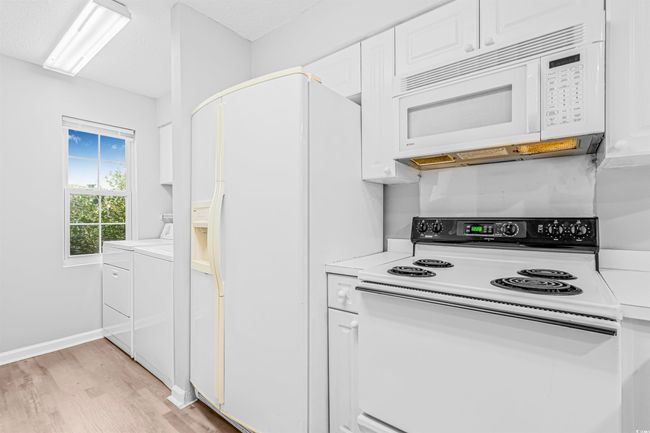 Kitchen with white appliances, white cabinets, light wood finished floors, and light countertops | Image 8