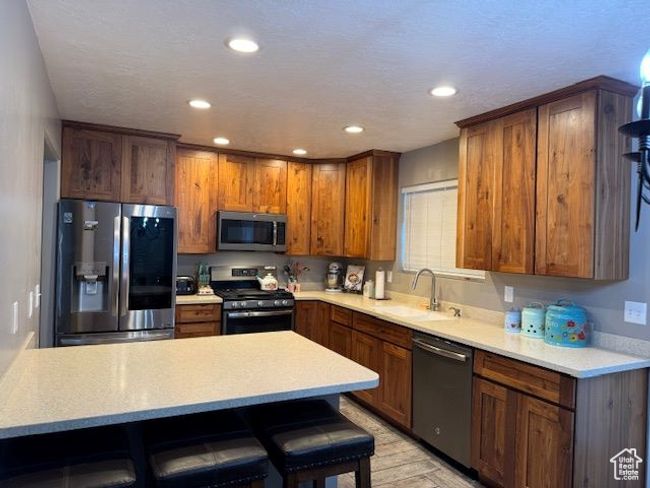 Kitchen featuring light countertops, appliances with stainless steel finishes, brown cabinetry, a sink, and a kitchen bar | Image 18