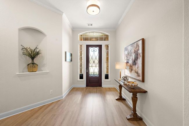 Elegant entryway showcasing a covered archway and decorative shelving, setting the tone for stylish living. The warm wood-inspired flooring leads guests seamlessly into the entertainment areas, enhancing the inviting atmosphere of this Spring Trails home. | Image 11