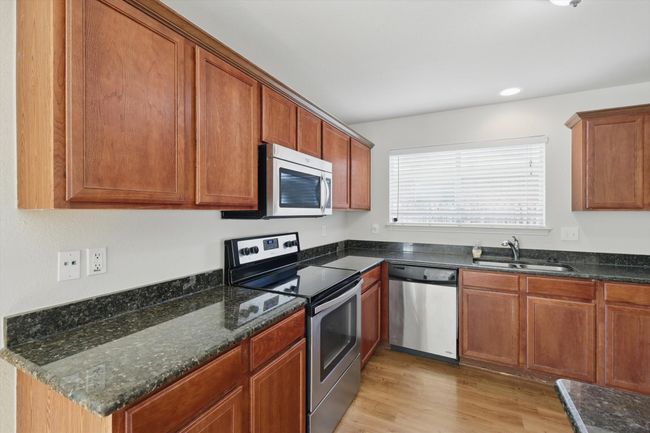 Kitchen with appliances with stainless steel finishes, a sink, light wood-style flooring, brown cabinetry, and dark stone countertops | Image 7