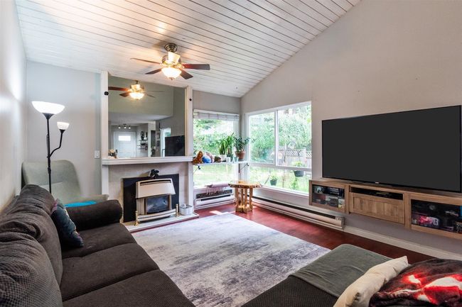 Living room featuring vaulted ceiling, wood finished floors, a ceiling fan, a baseboard heating unit, and a tile fireplace | Image 6