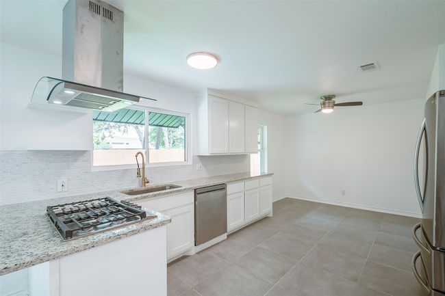 Kitchen featuring appliances with stainless steel finishes, island exhaust hood, decorative backsplash, a ceiling fan, and white cabinets | Image 13