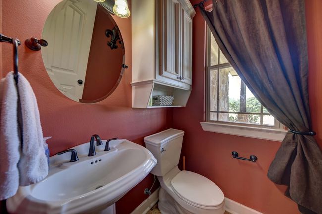 This cozy half bathroom features a pedestal sink with a round mirror and a window with natural light. | Image 28